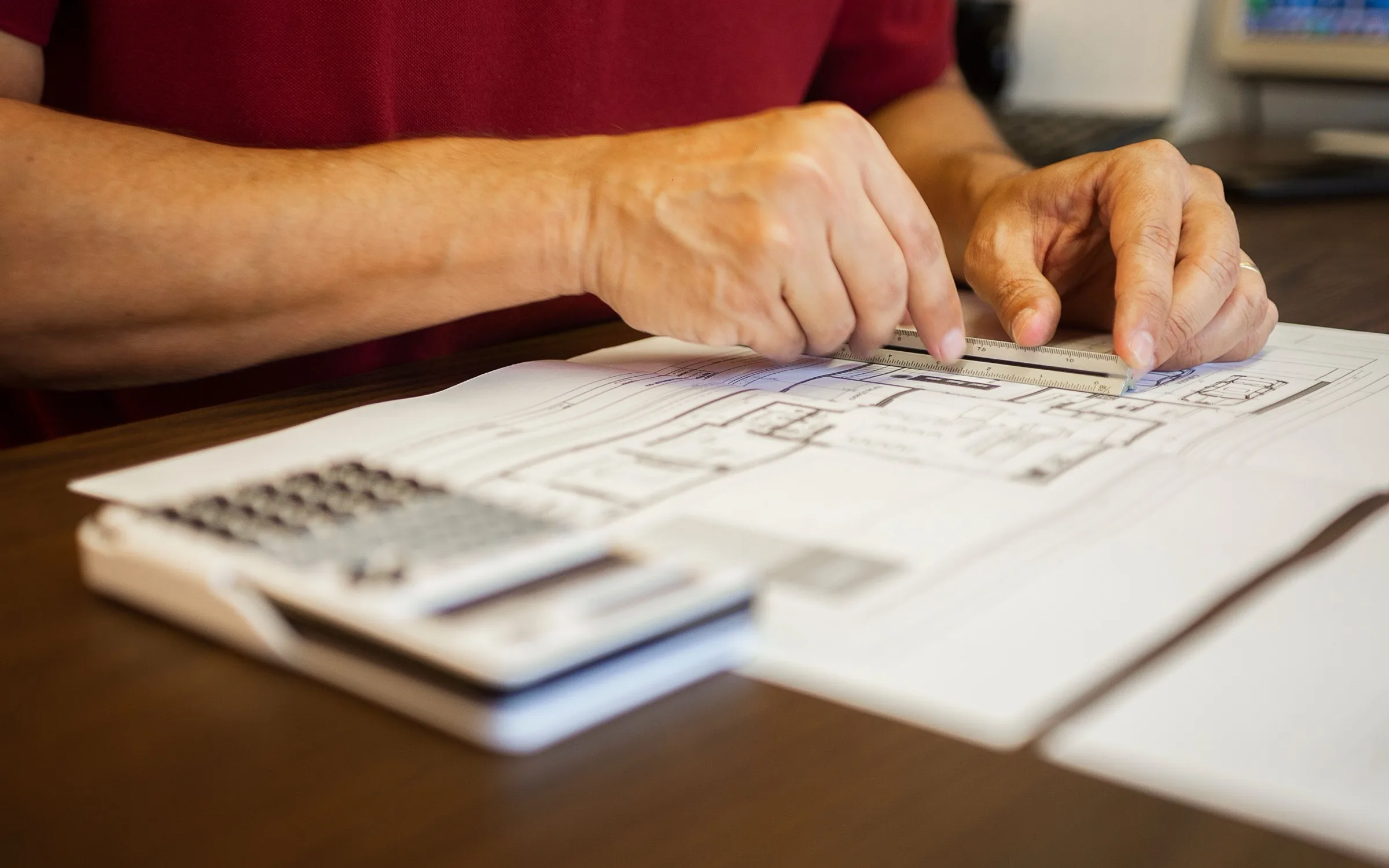 An estimator checking a drawing with a scale rule and a calculator at a desk