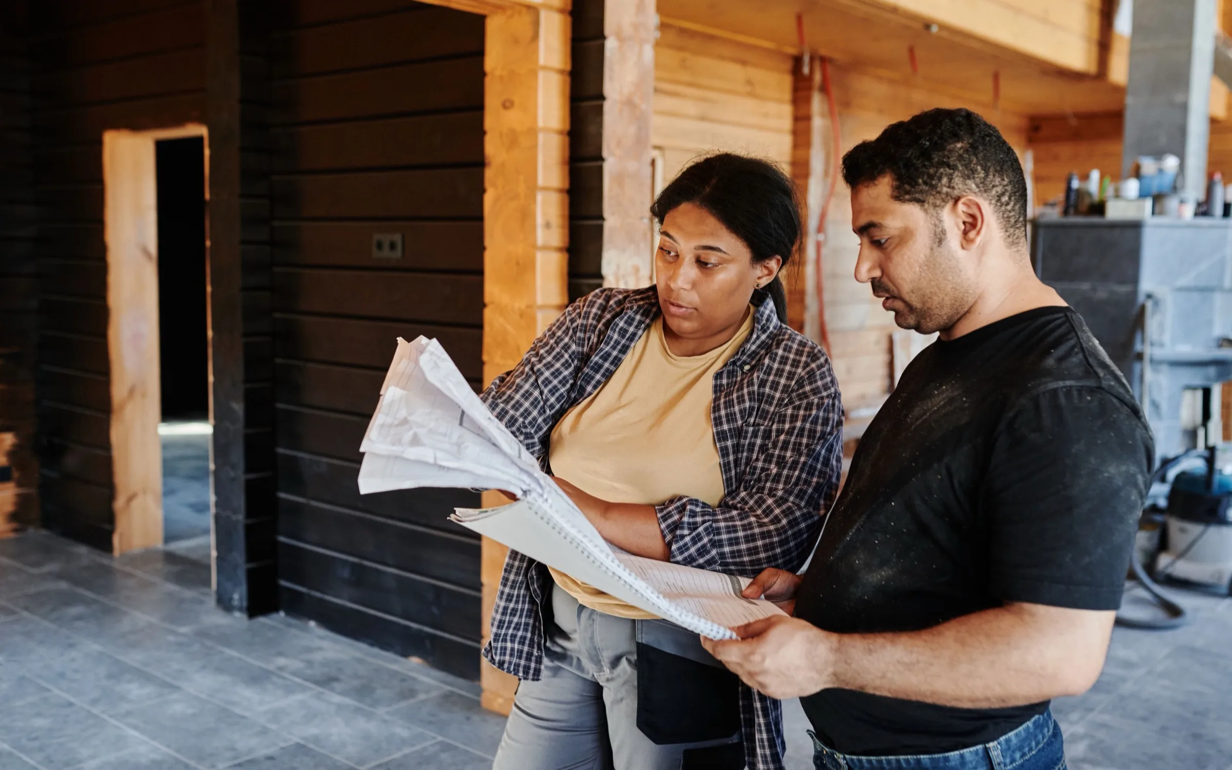 A general contractor and a subcontractor reviewing plans together inside a wood-clad structure
